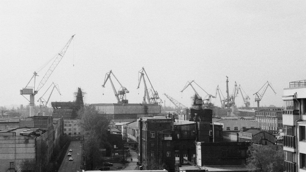 Black and white cityscape of industrial cranes in an urban setting.