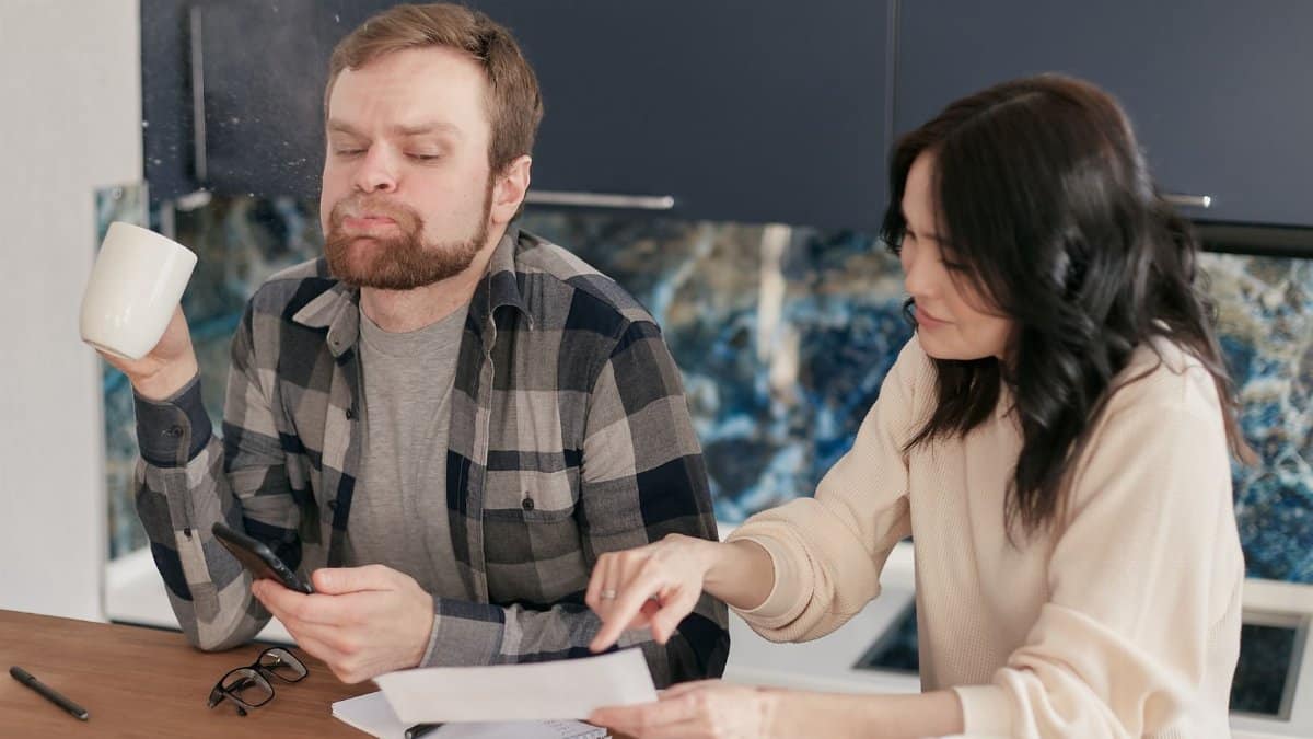 A couple reviews bills at their kitchen table, looking concerned and thoughtful.