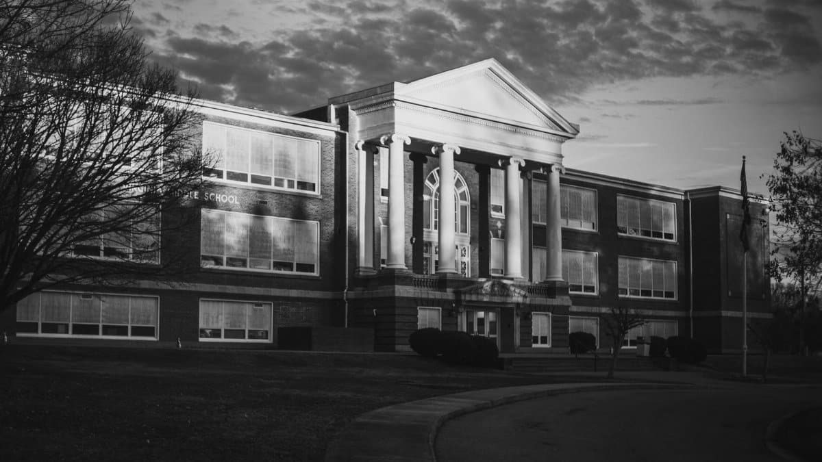 Classic black and white photo of a historic school building with dramatic lighting at dusk.