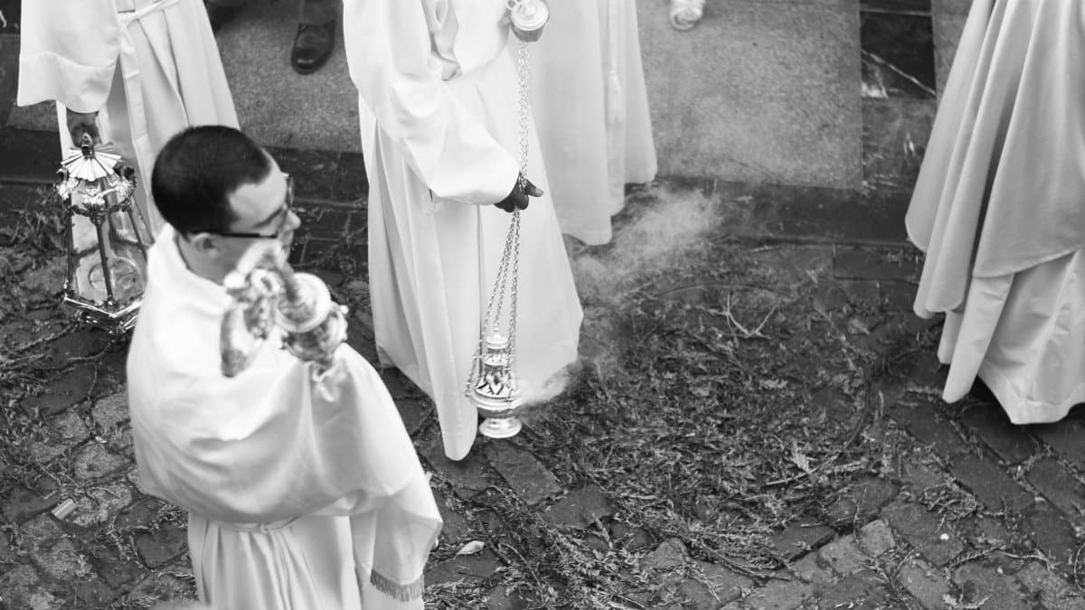 Black and white photo of a religious procession with priests carrying incense outdoors.