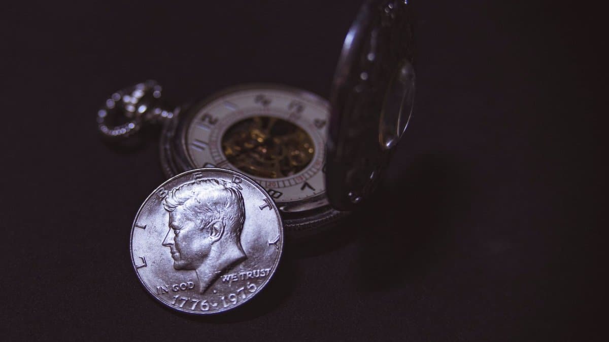 Close-up of a vintage silver coin with a pocket watch, symbolizing time and wealth.