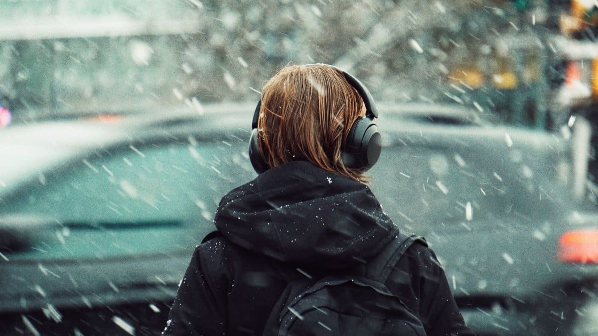 Person with headphones walks through snowy city street, winter scene.