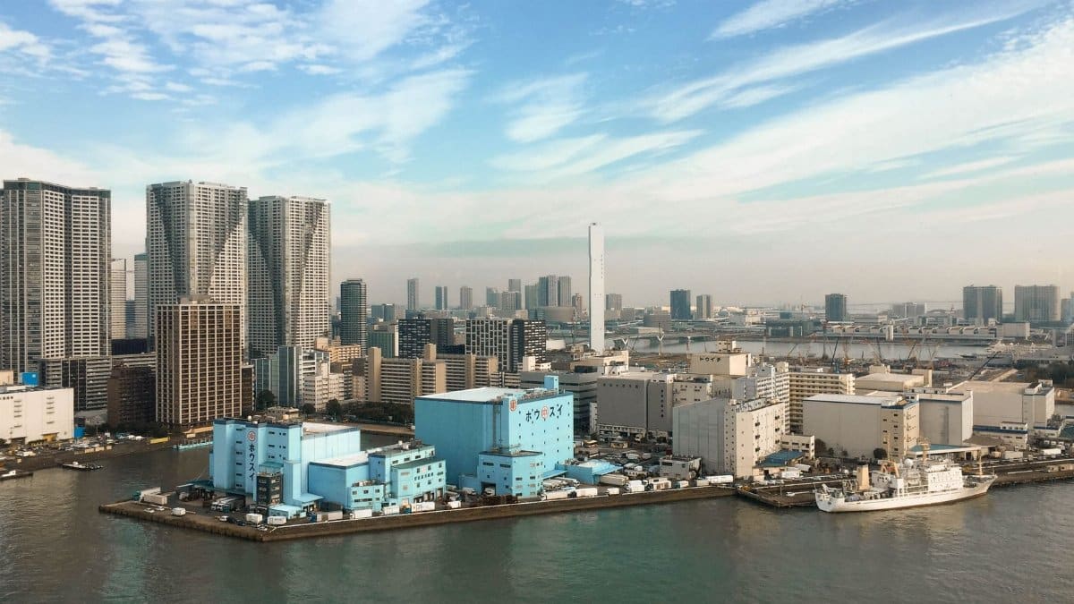 Aerial view of a modern city skyline with skyscrapers and waterfront buildings under a clear blue sky.