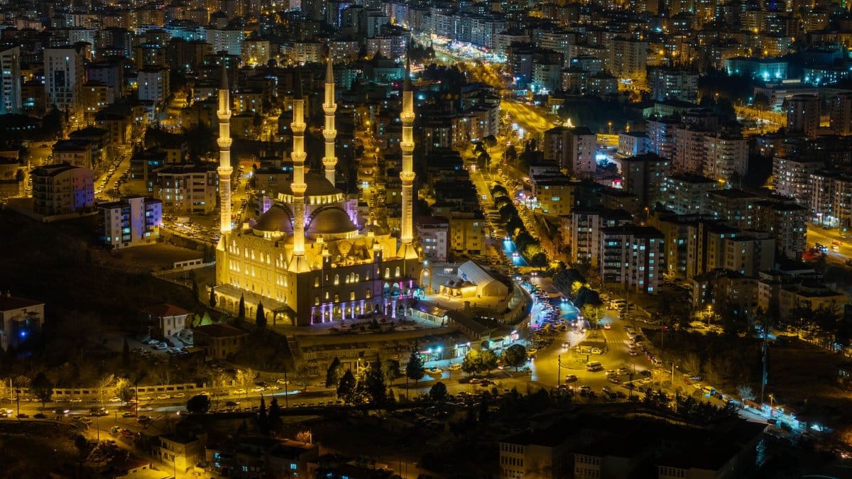 Nighttime aerial view of a brightly lit mosque surrounded by city lights in Kahramanmaraş, Turkey.