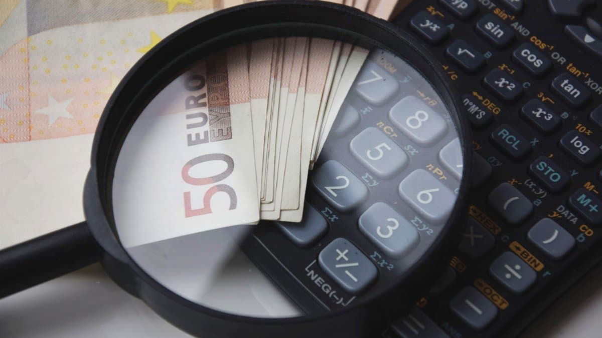 Euro bills under magnifying glass with calculator, symbolizing finance and analysis.