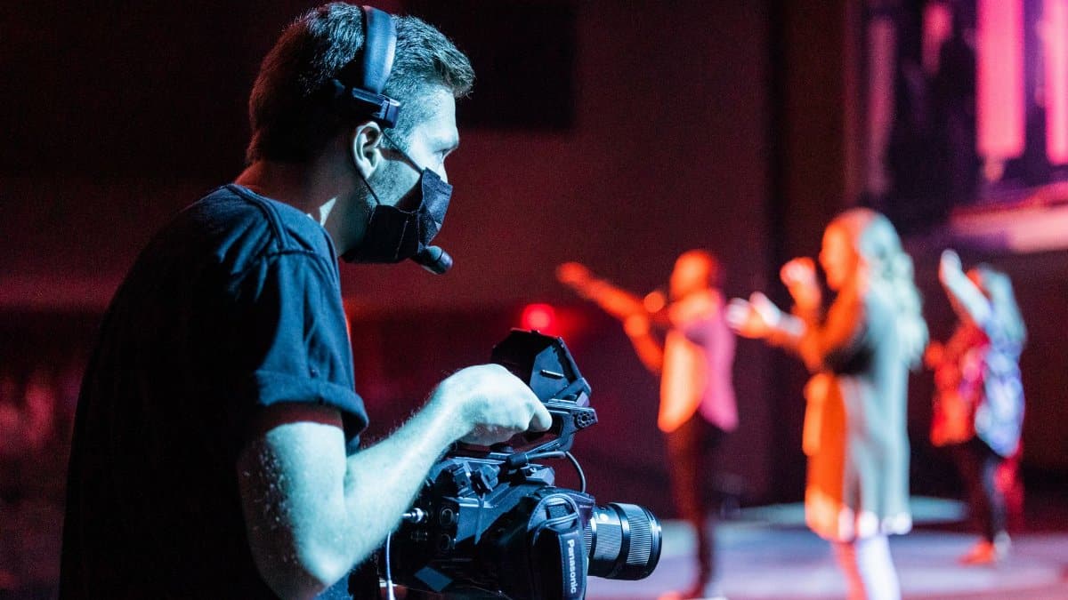 A videographer captures a live stage performance, using professional equipment indoors.