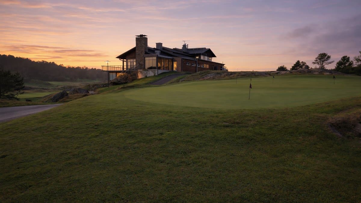 A tranquil golf course with a modern clubhouse under a vibrant sunset sky.
