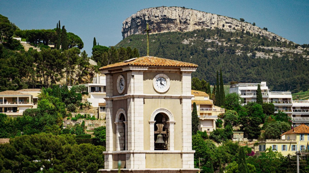 Picturesque clock tower in Cassis, France, against lush hillside and sunny skies.