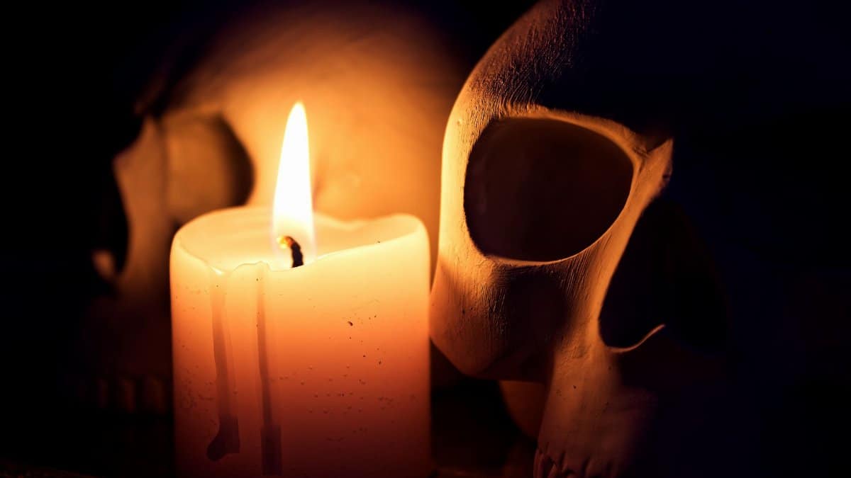 A dramatic still life featuring a candle illuminating two human skulls in the dark.