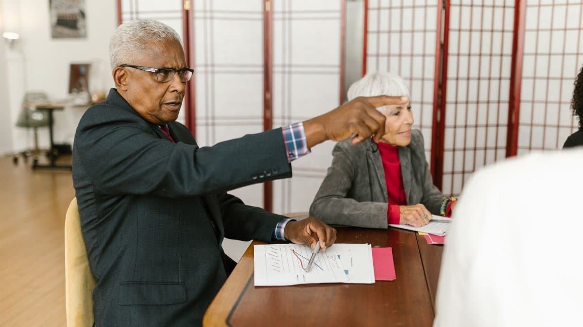 Elderly professionals collaborate in a meeting, discussing documents on a wooden table.