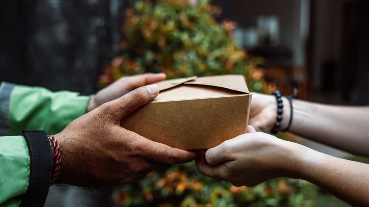 Close-up of hands exchanging a cardboard box, symbolizing delivery service outdoors.