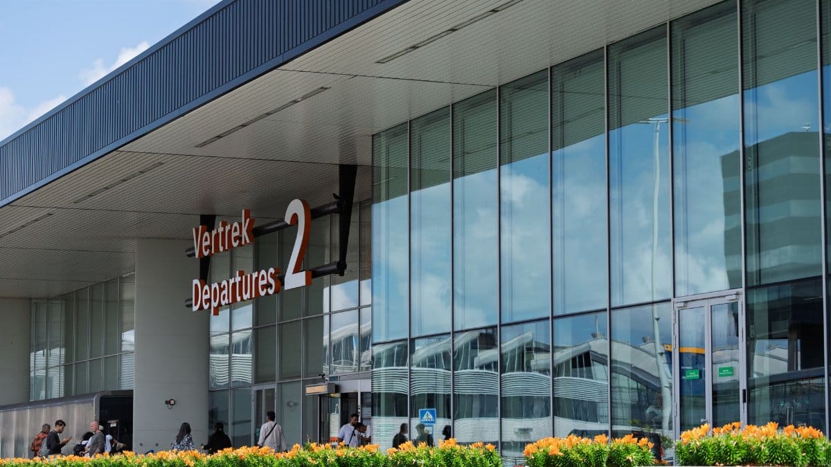 Glass facade of a bustling airport departure terminal with people outside and reflection of clouds.