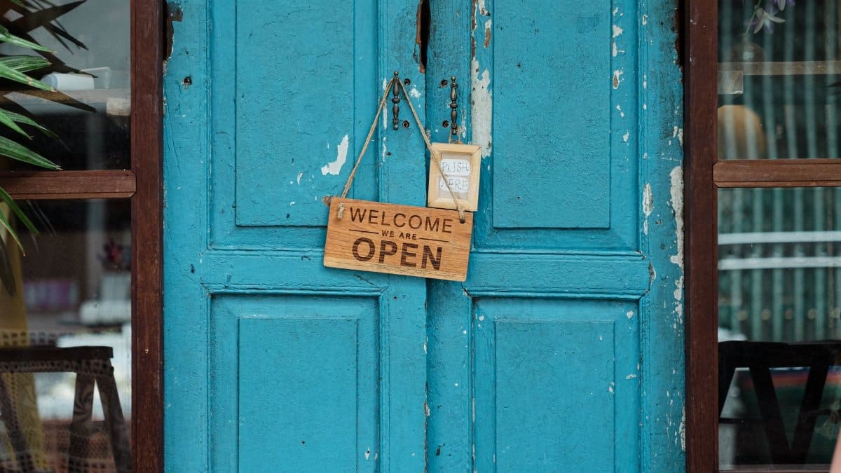 A rustic blue door with a wooden welcome sign indicating the store is open.
