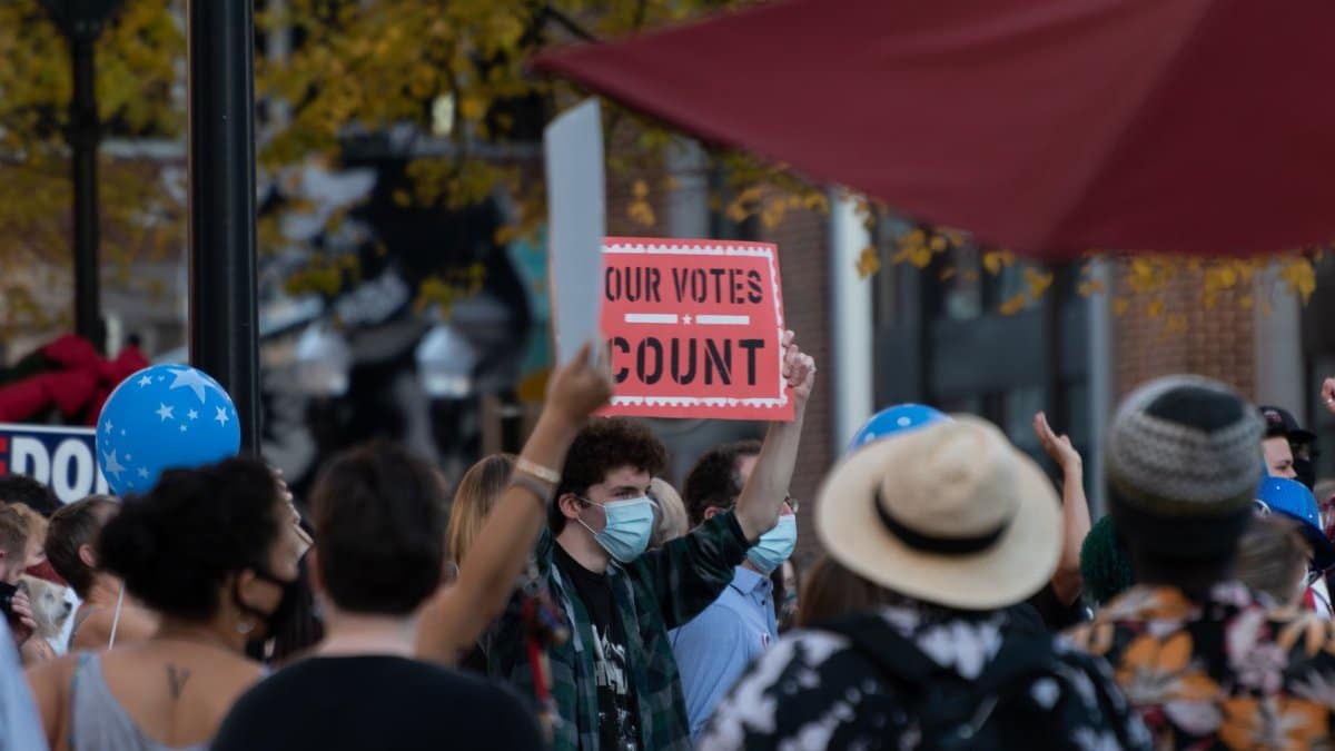 A group of protesters holding a sign promoting vote counting. Diverse adults in an outdoor setting.