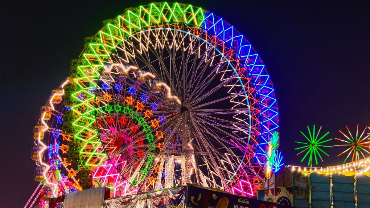 Vibrant neon-lit Ferris wheel at a night fair in Porbandar, India, showcasing dazzling colors.