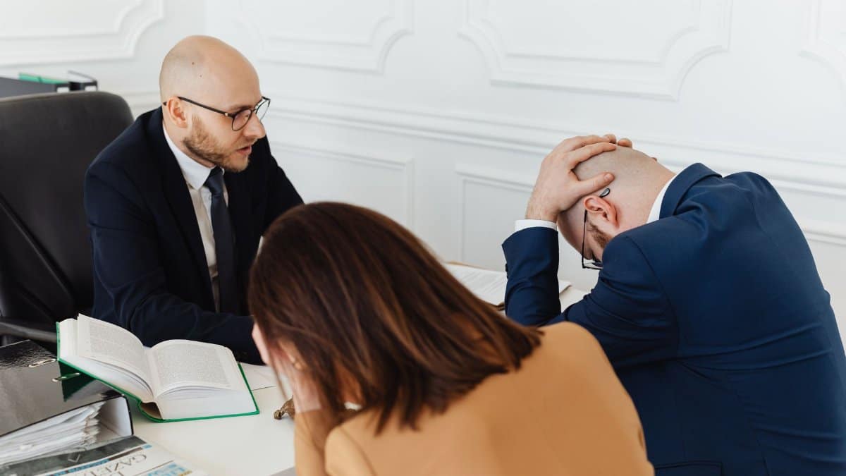 Legal professionals engaged in a tense meeting at a law office with open documents on the desk.