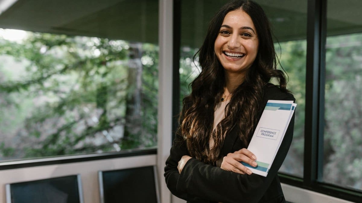 Confident woman holding conference program, smiling in modern indoor setting.