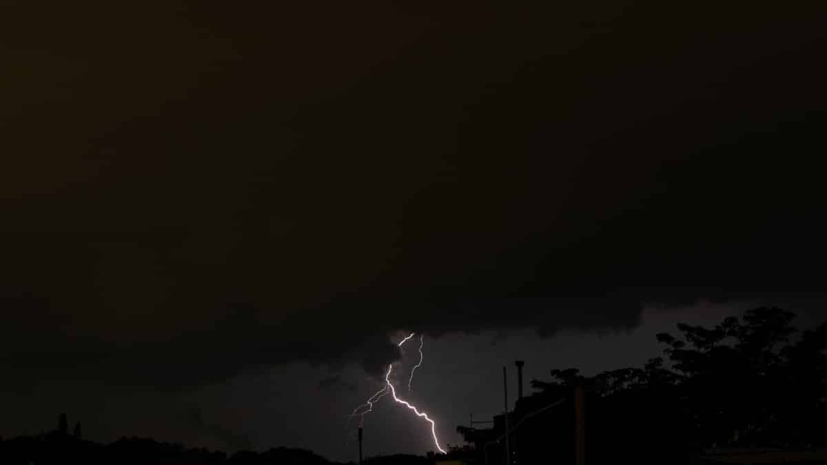 Dramatic night scene capturing a single lightning bolt piercing through dark thunderclouds over a silhouetted landscape.
