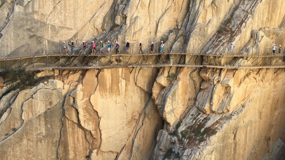 Adventurers walking the narrow Caminito del Rey path against stunning cliff backdrop in Spain.