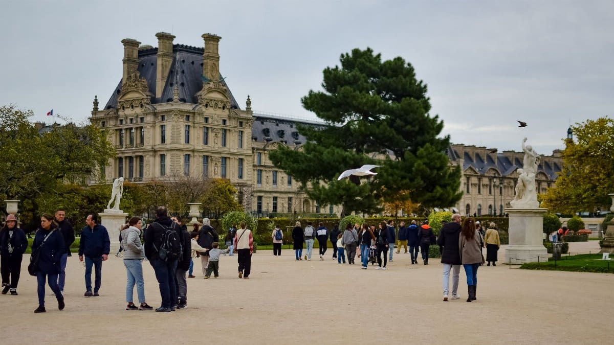 Visitors enjoying a leisurely walk in Tuileries Garden with classic architecture in the background.