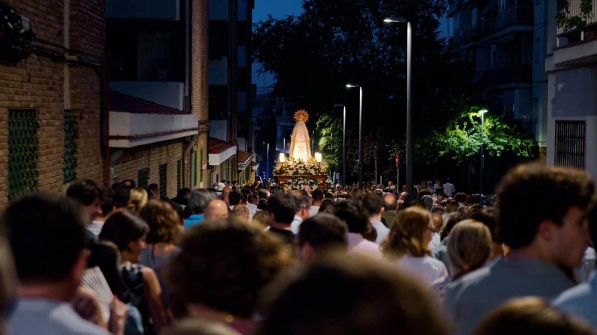 A bustling night street procession with a religious figure, highlighting urban faith and community gathering.