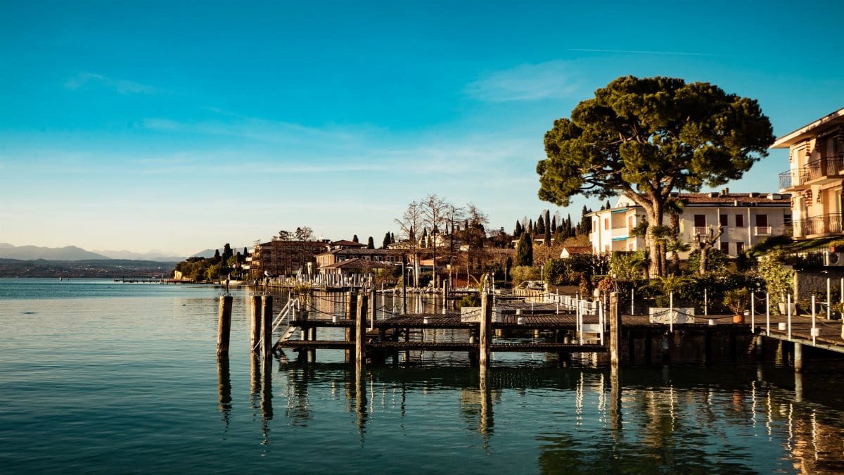 Beautiful waterfront town by a lake with reflections of buildings, trees, and a pier under clear blue skies.
