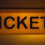 Close-up of an illuminated yellow ticket sign against a dark background.