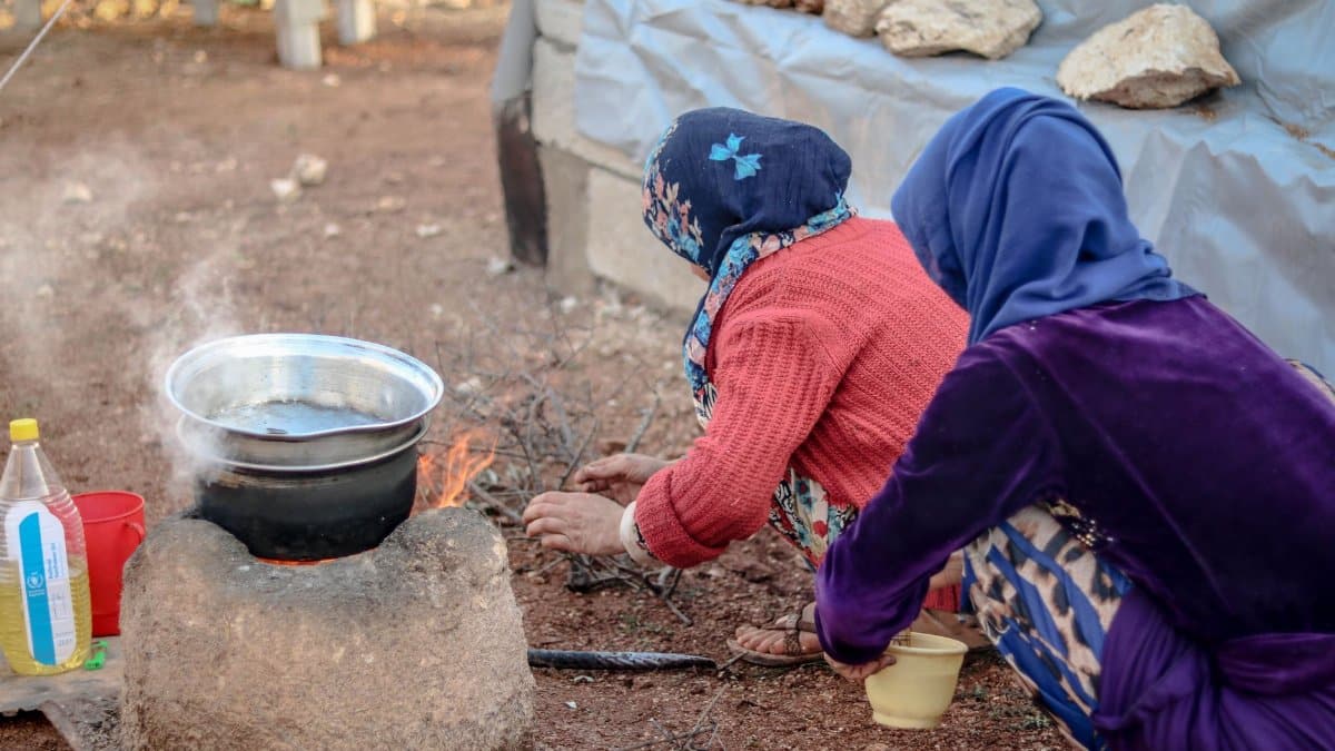 Two women cooking over an outdoor fire in Idlib, Syria, highlighting rural life and traditional practices.