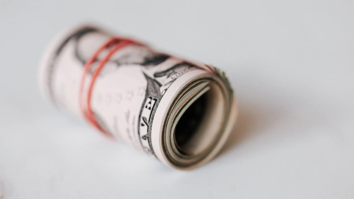 High angle roll of five dollar bills on white table tightened with red rubber band