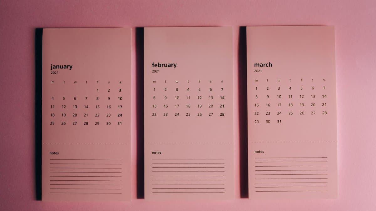 Overhead view of modern paper calendars with horizontal lines for notes and monthly dates on pink background