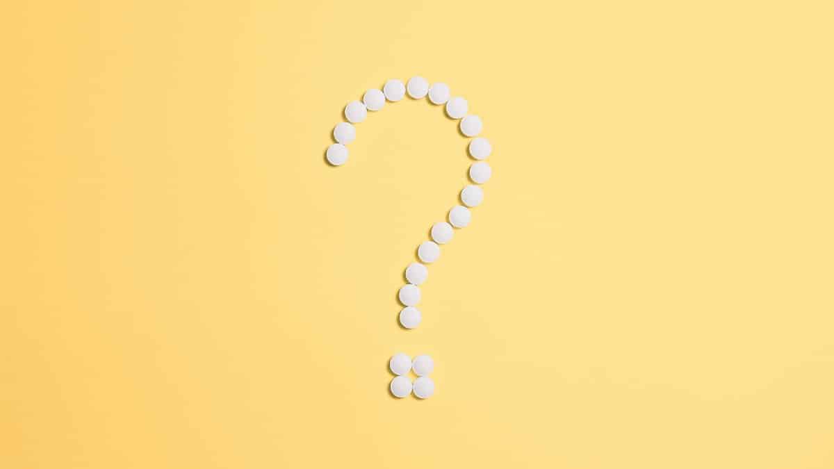 White pills arranged into a question mark shape on a vibrant yellow background.