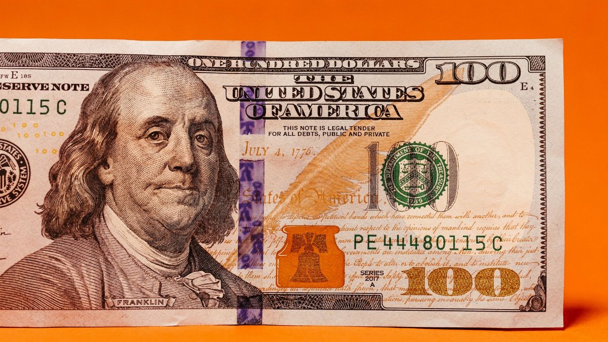 Detailed image of a US hundred dollar bill against a vibrant orange background.