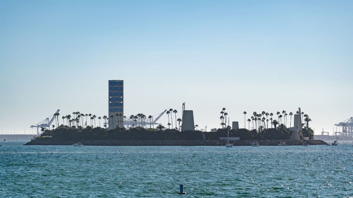 Silhouetted palm trees and oil rig on an island in the ocean with a clear blue sky.