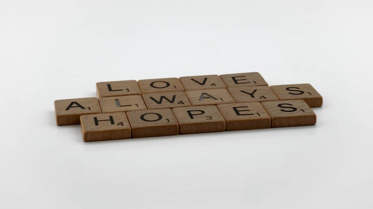 A thoughtful message spelled with Scrabble tiles on a white surface, conveying hope and love.