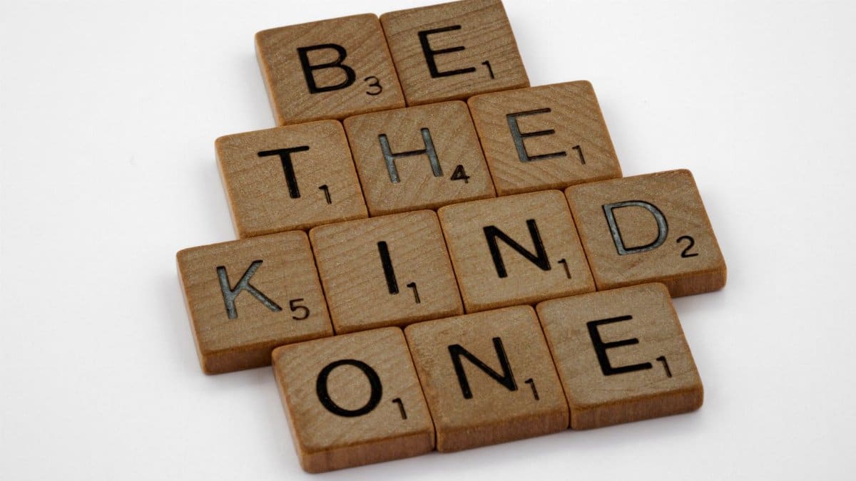 Scrabble tiles arranged to spell 'BE THE KIND ONE' on a white background, emphasizing kindness.
