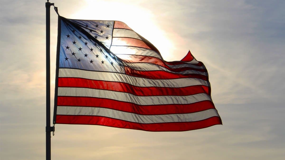 A sunlit American flag waves gracefully against a bright sky in Minnesota, USA.