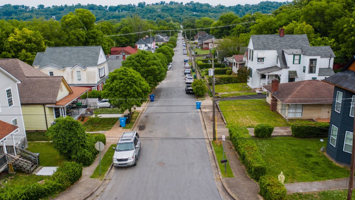 Explore a quiet suburban neighborhood street with houses and lush greenery from an aerial perspective.