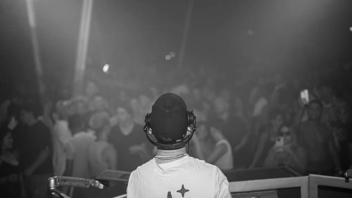 A DJ playing music in front of a vibrant crowd at a night concert.