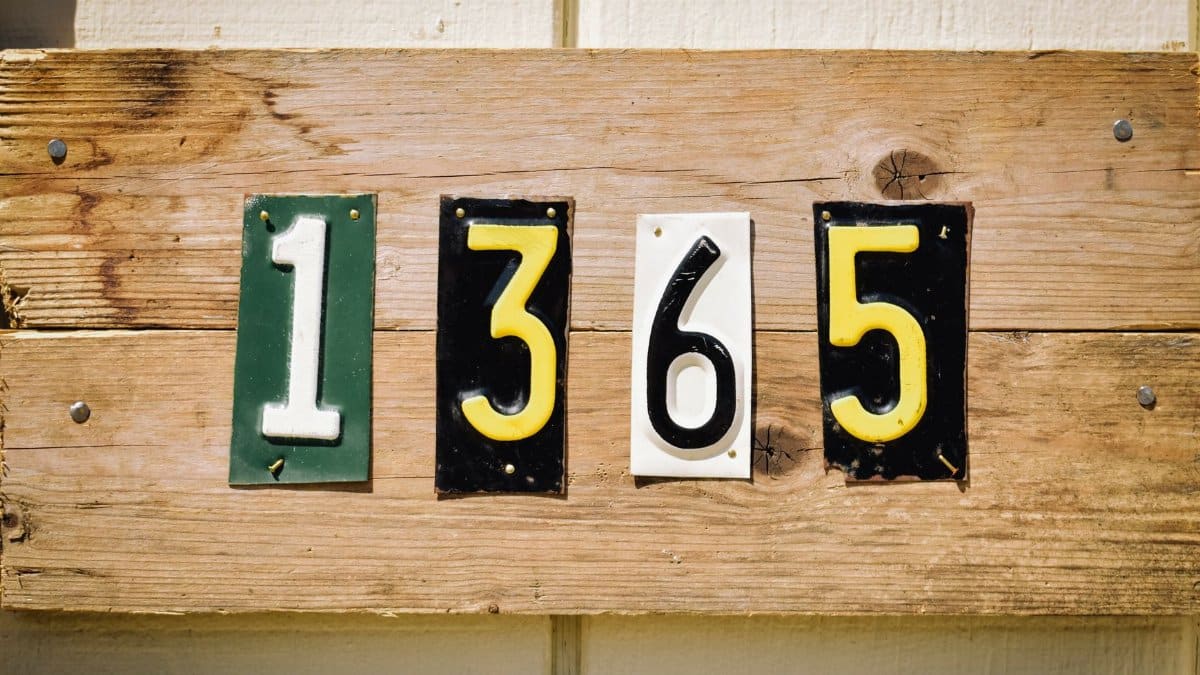 Rustic wooden house number sign with colorful digits 1365 on weathered planks, outdoors.