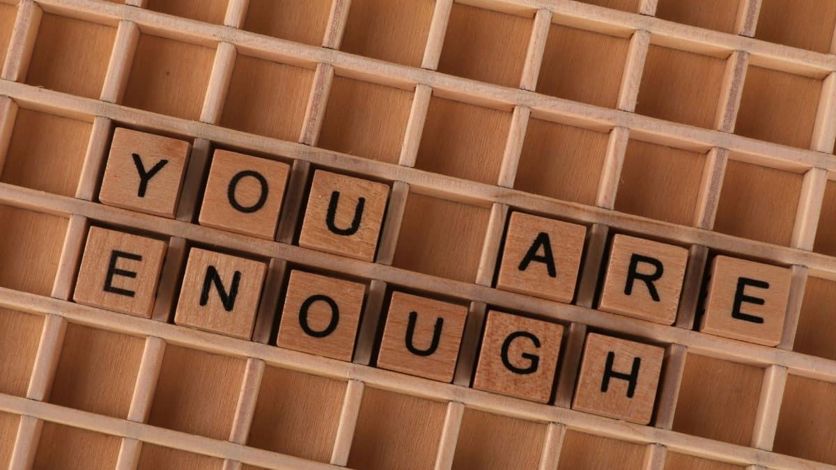Motivational quote 'You Are Enough' spelled using wooden letter tiles on a wooden grid.