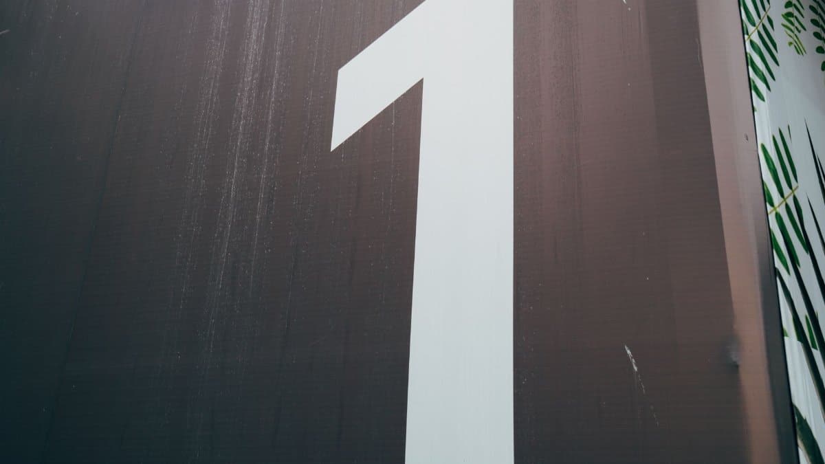 A close-up image of a large, white number one painted on a dark wall.
