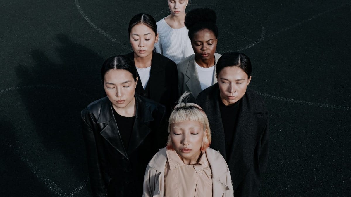 A diverse group of women standing together with eyes closed in a fashion-themed portrait taken from above.