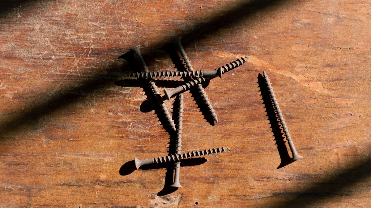 Close-up of rusty screws scattered on a wooden surface with dramatic shadows.