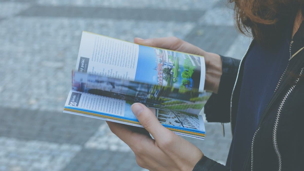 A person flipping through a travel book outdoors, showcasing a variety of vibrant pages.