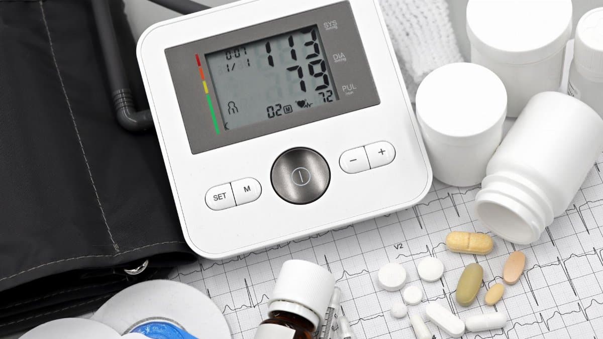 Digital blood pressure monitor on ECG paper with pills and medical supplies, ideal for healthcare topics.