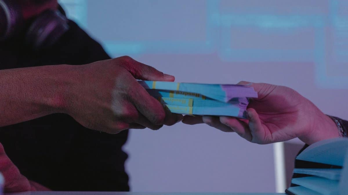 Close-up of hands exchanging money, highlighting financial exchange in a dimly lit setting.