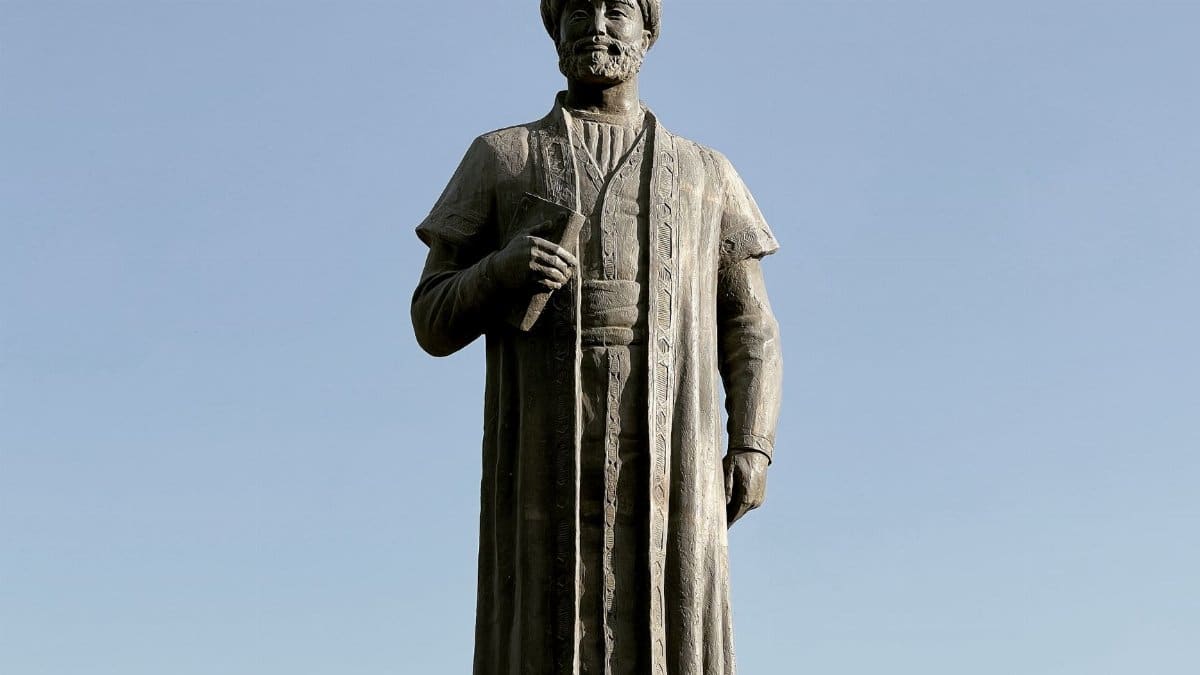A stone statue of a historic figure holding a book stands under a clear blue sky.