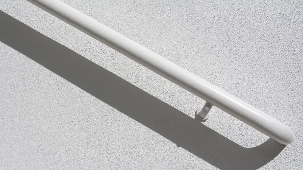 A white handrail casting a shadow on a textured wall in a minimal, abstract composition.