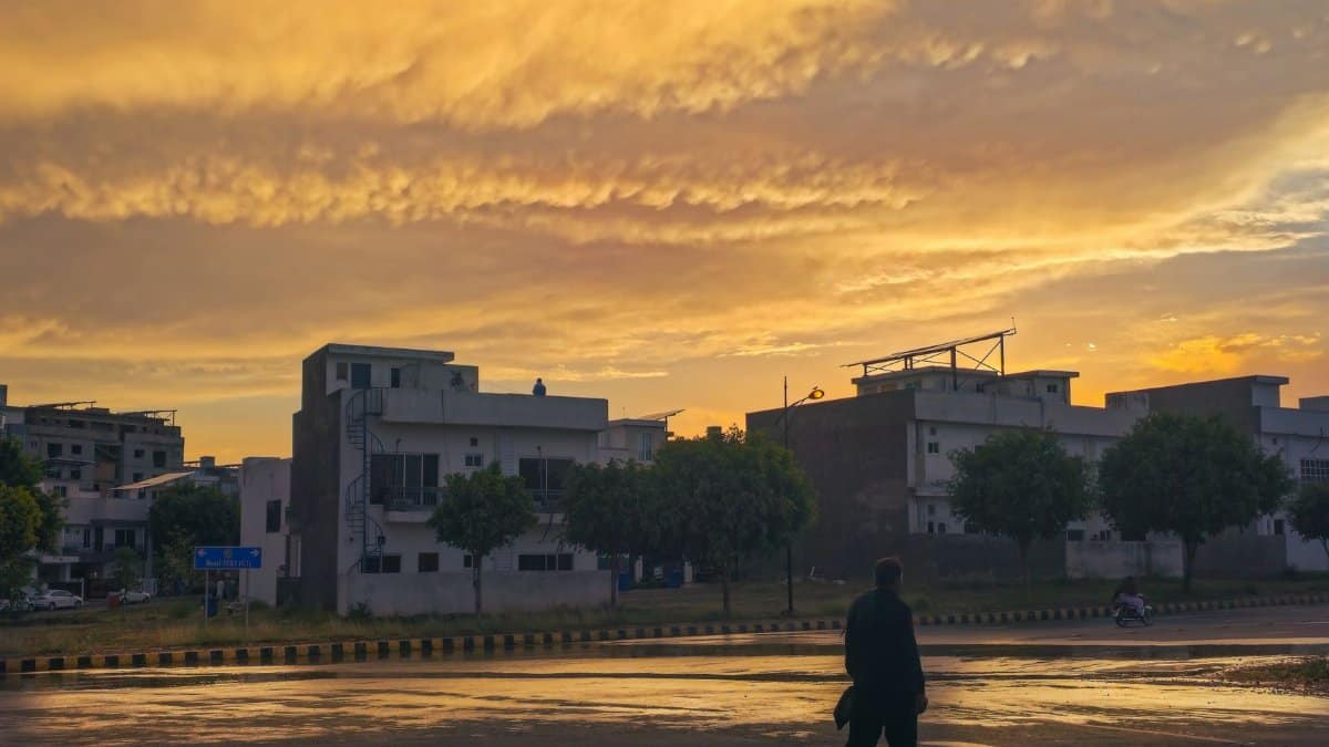 A silhouette of a person walking on a wet street under a dramatic sunset sky in an urban setting.