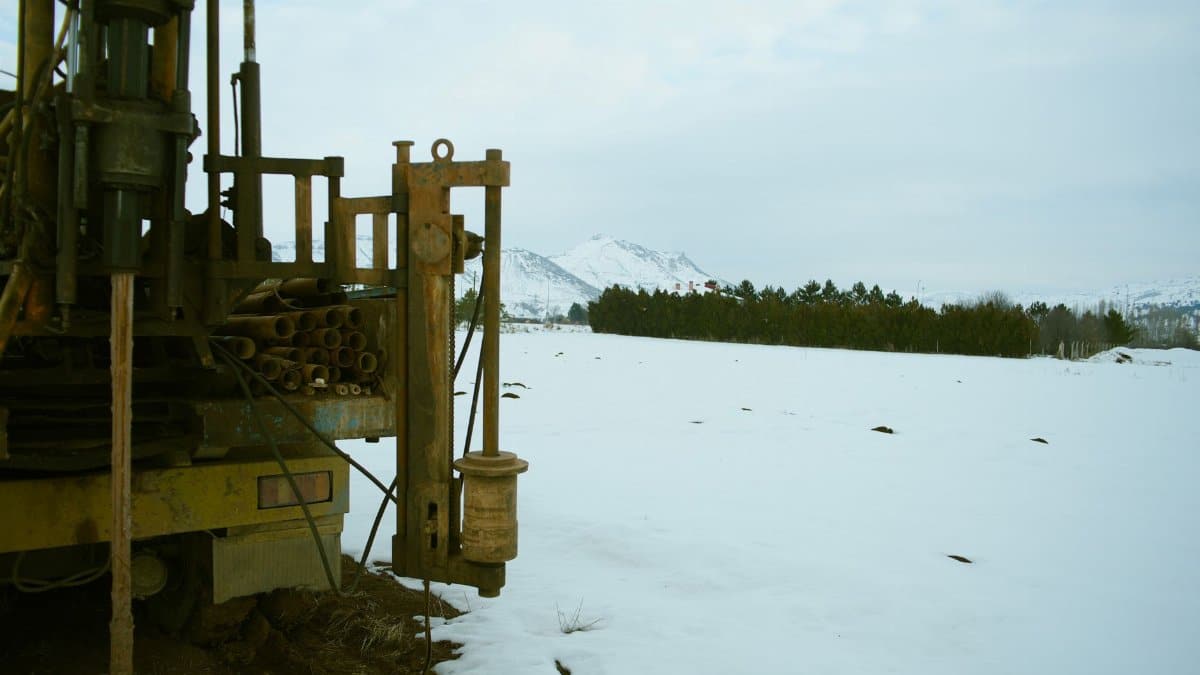 A large industrial drill machine set against a snowy winter landscape with mountains in the background.